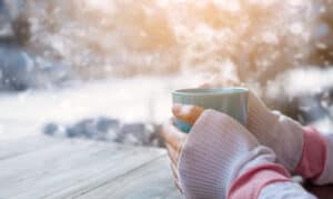 woman warming her cold hands over a cup of hot tea